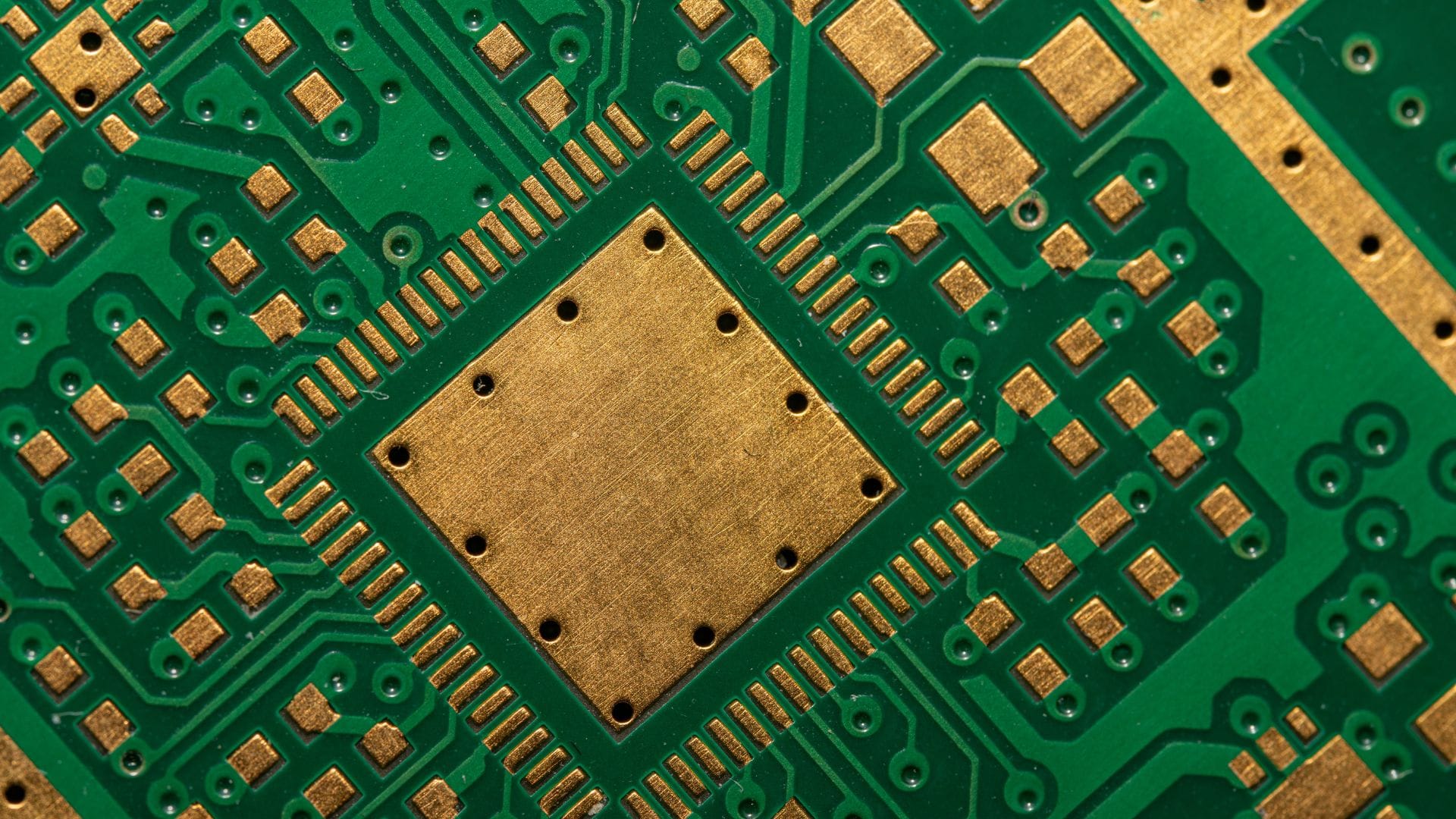Detailed view of a green printed circuit board (PCB) with gold pads and intricate electrical pathways.