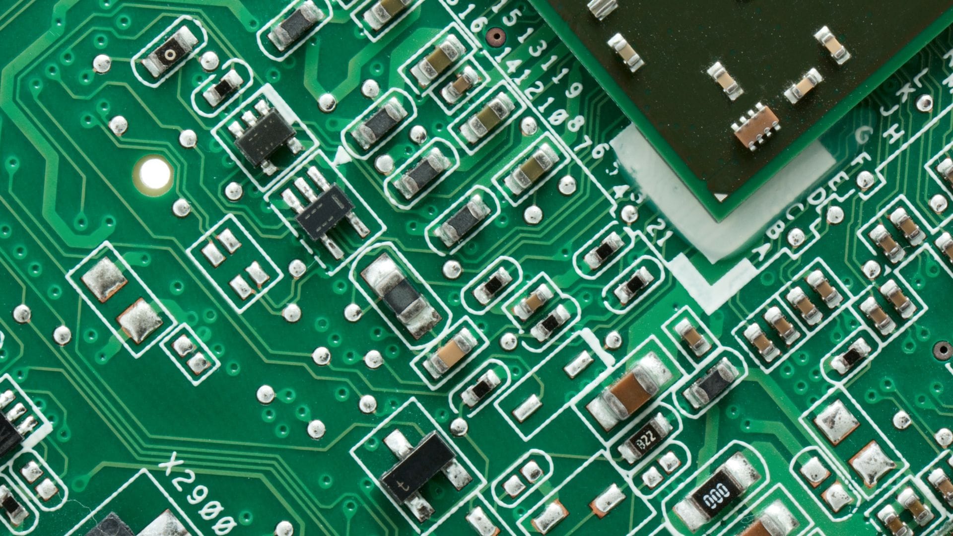 Close-up of a densely populated green circuit board with microchips, resistors, and traces.