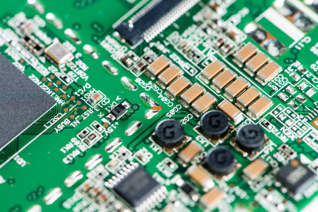 Close-up macro photograph of a green printed circuit board (PCB) showing electronic components, microchips, capacitors, and soldered connections with shallow depth of field.